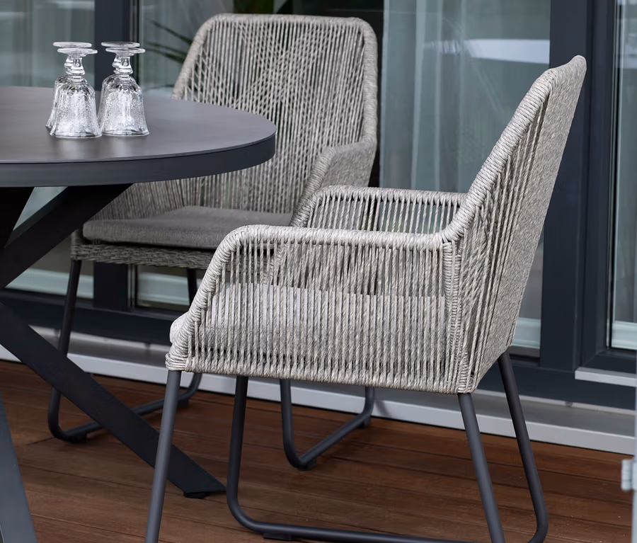 Zwei deVries 2 Dining-Sessel und ein Tisch mit zwei Gläsern auf einer Terrasse.
