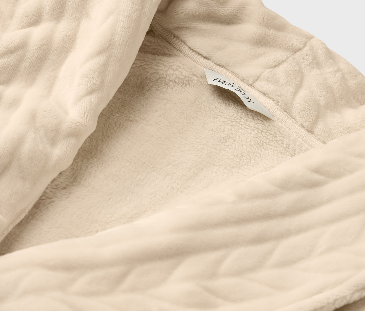 Detailaufnahme eines cremefarbenen Bademantels mit Textur und dem Etikett "everybody".
