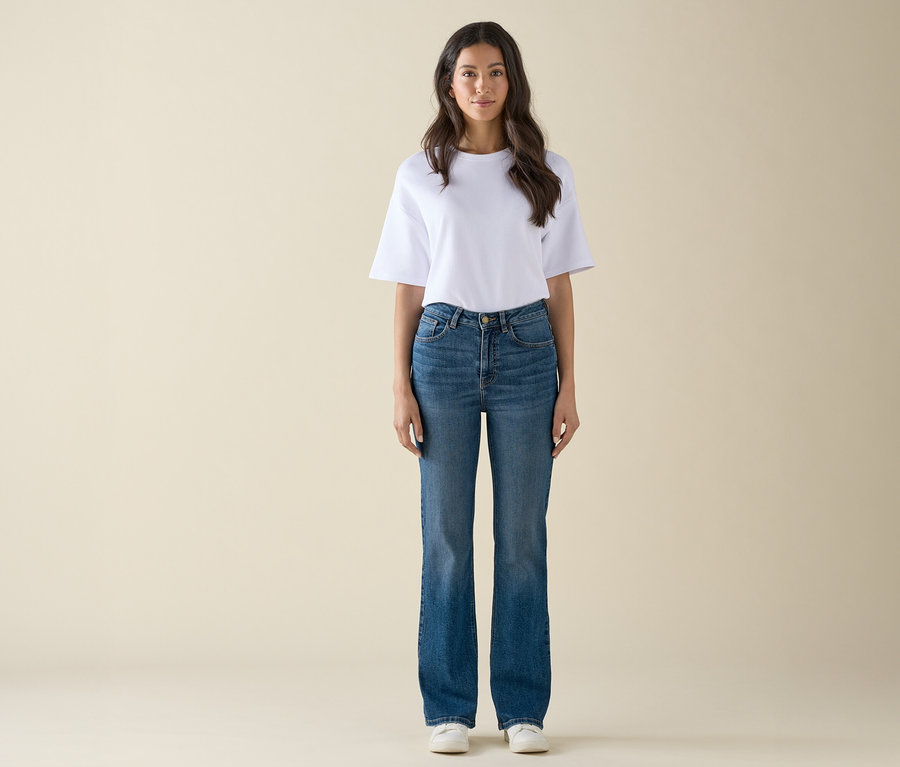 Eine Frau steht und trägt ein weißes T-Shirt, blaue Jeans und weiße Turnschuhe.