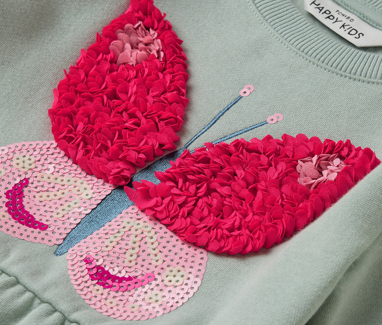 Hellgrünes Kleid mit Schmetterlingsapplikation mit rosa Pailletten und roten Blüten.