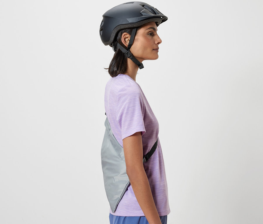 Seitliche Aufnahme einer Frau mit Fahrradhelm, die eine Fahrrad-Einkaufstasche über der Schulter trägt.