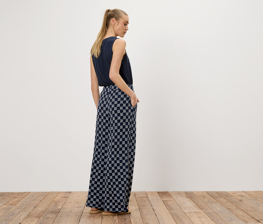 Eine Frau steht mit dem Rücken zur Kamera, trägt ein marineblaues Top und eine weite Hose mit einem weißen geometrischen Muster.