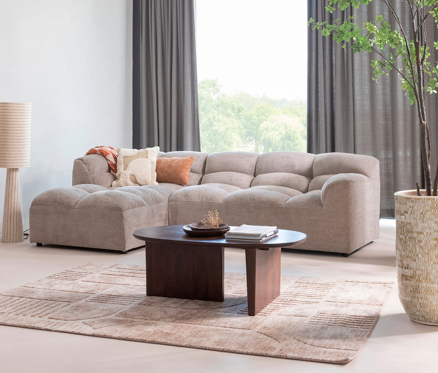 Wohnzimmer mit beigem Modulsofa, dunklem Couchtisch, gemustertem Teppich und Stehlampe.