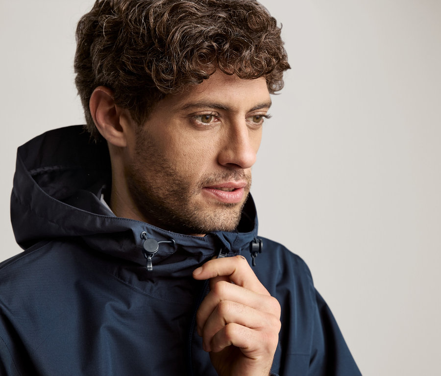 Mann mit lockigem Haar, der eine marineblaue Jacke mit Kapuze trägt.