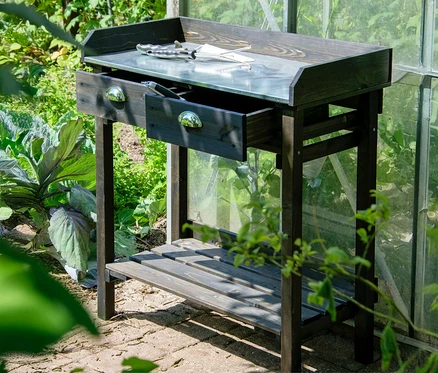 Ein schwarzer Pflanztisch mit Schubladen steht im Garten.