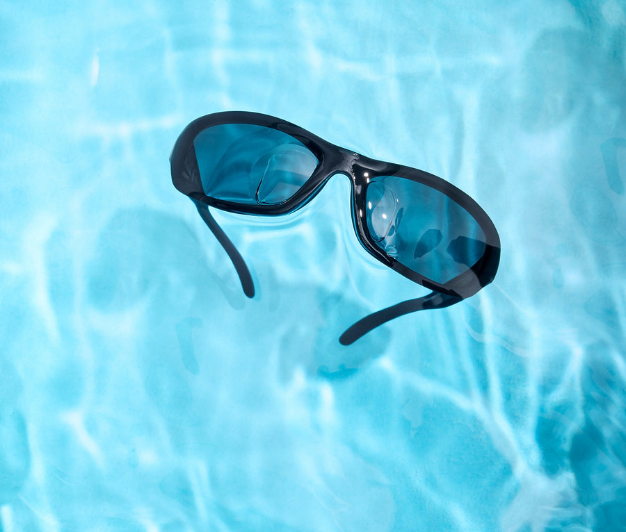 Schwarze Sonnenbrille schwimmt im hellblauen Wasser.