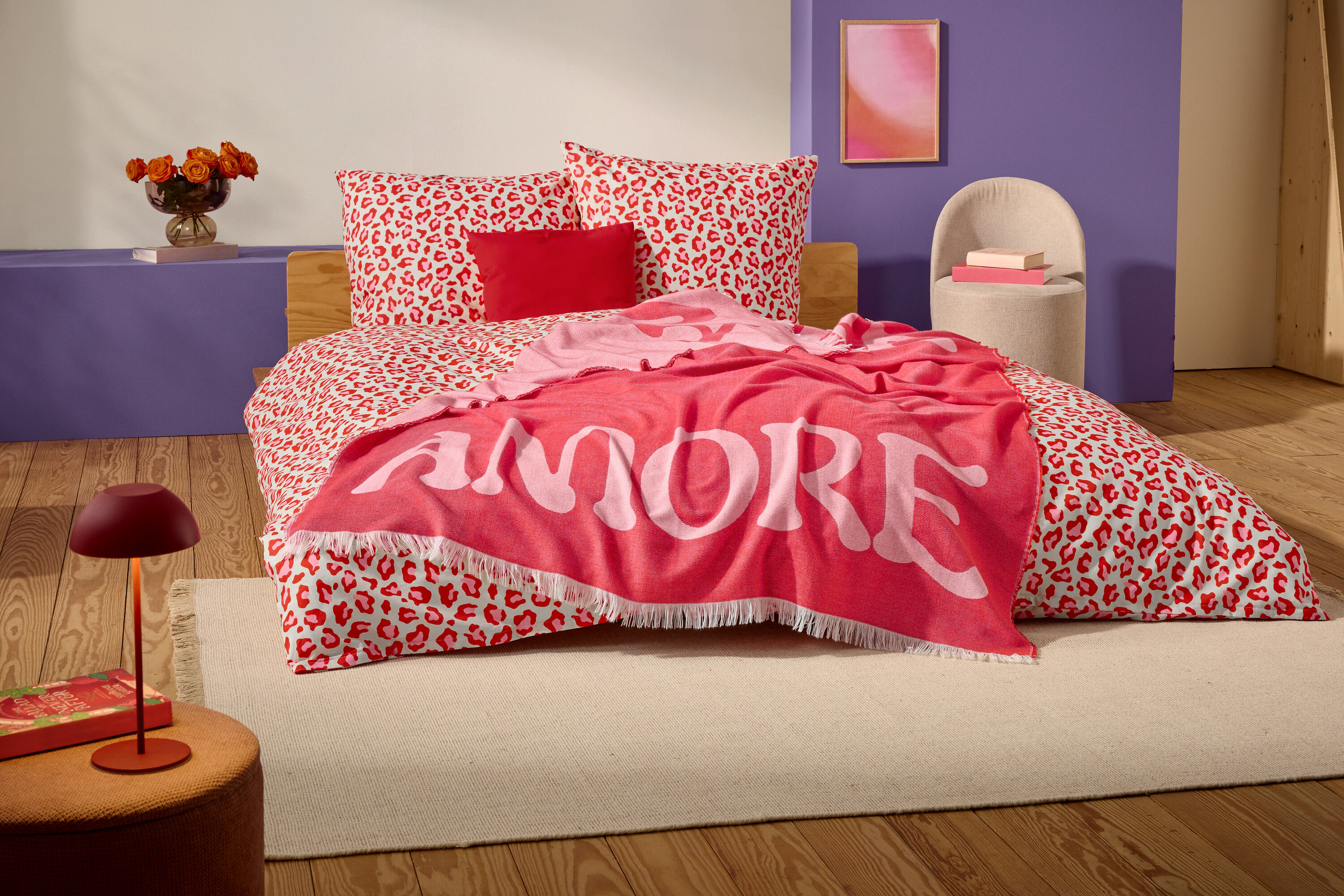 Auf einem Bett mit rot-weißem Leopardenmuster liegt eine rote Decke mit dem Wort "AMORE" in großen weißen Buchstaben.