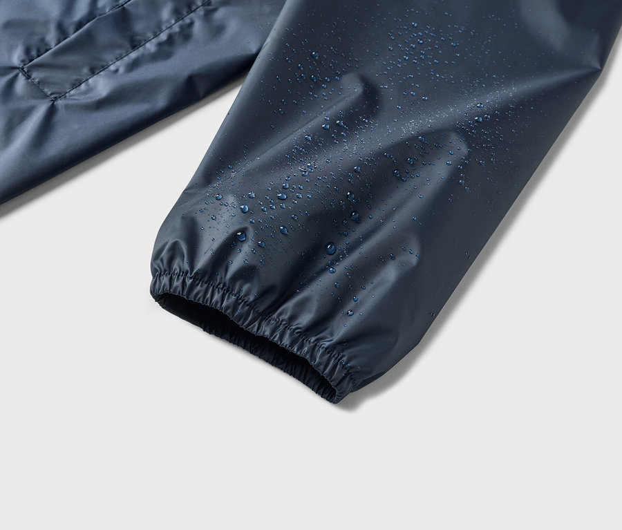 Nahaufnahme eines Ärmels einer wasserabweisenden, marineblauen Jacke, auf dem sich Wassertropfen befinden.