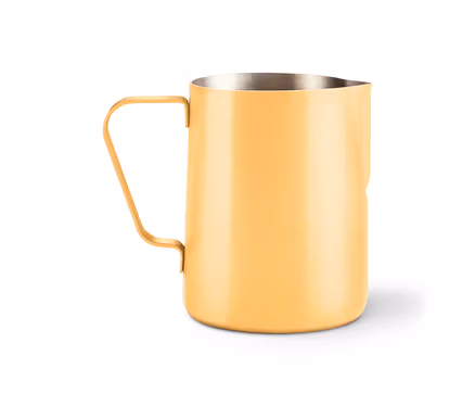 Gelber Milchkrug aus Metall mit Griff und Ausguss steht auf einem weißen Untergrund.