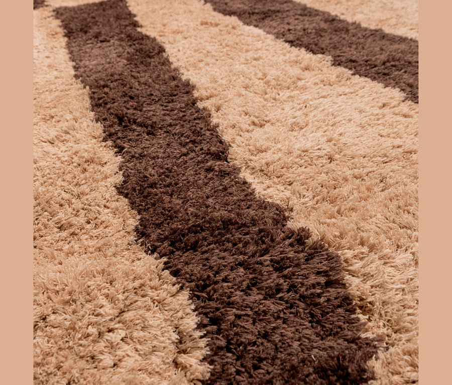 Nahaufnahme eines Hochflor-Teppichs mit wellenförmigen, diagonalen Streifen in Braun und Beige.
