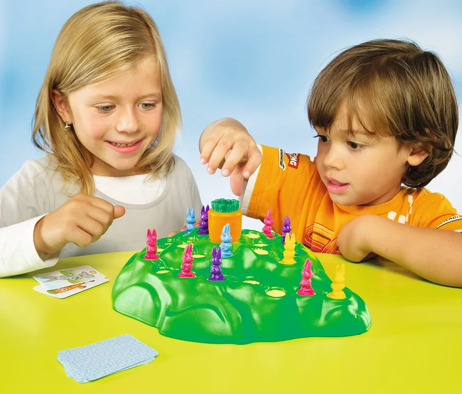 Kinder spielen das Spiel Ravensburger »Lotti Karotti« mit bunten Hasenfiguren auf einem grünen Hügel.