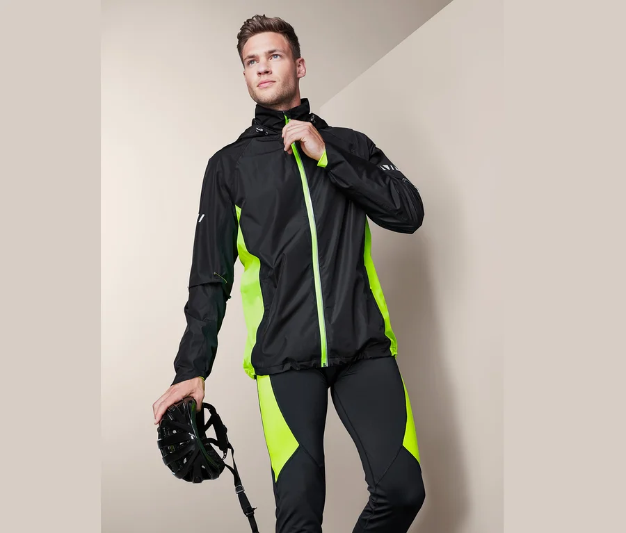 Mann schliesst eine schwarze Velo-Regenjacke mit neongrünen Details und hält einen Velohelm.