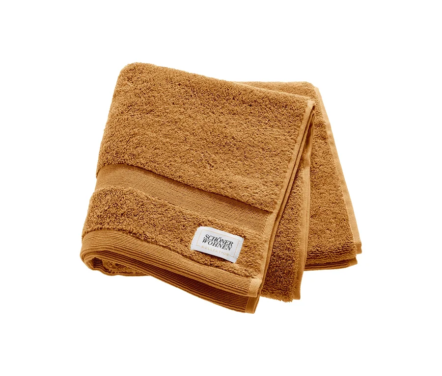 Ein braunes, gefaltetes Handtuch der SCHÖNER WOHNEN-Kollektion mit einem weißen Markenetikett.