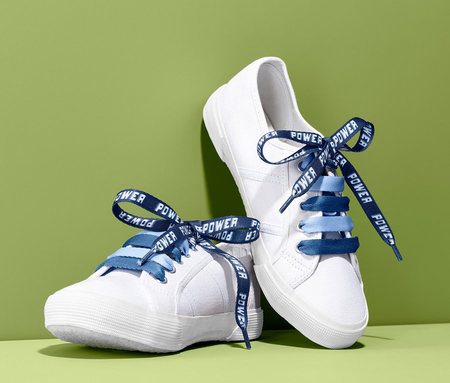 Zwei weiße Schuhe mit blauen Kinder-Schnürsenkel mit Motiv auf grünem Hintergrund.