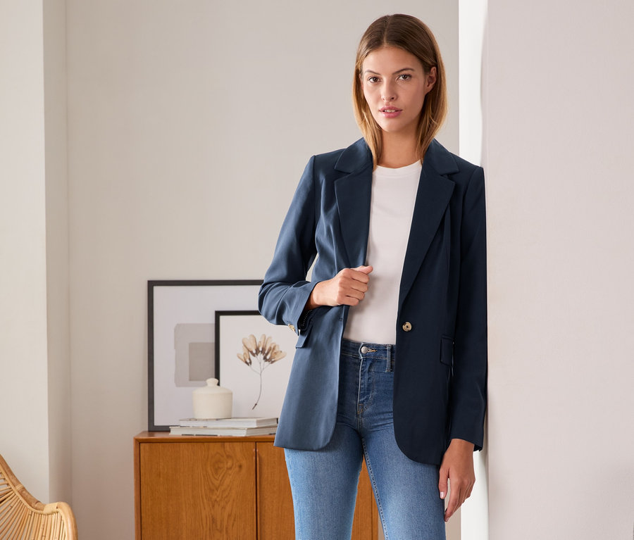 Frau posiert in Webblazer, Jeans und Turnschuhen.