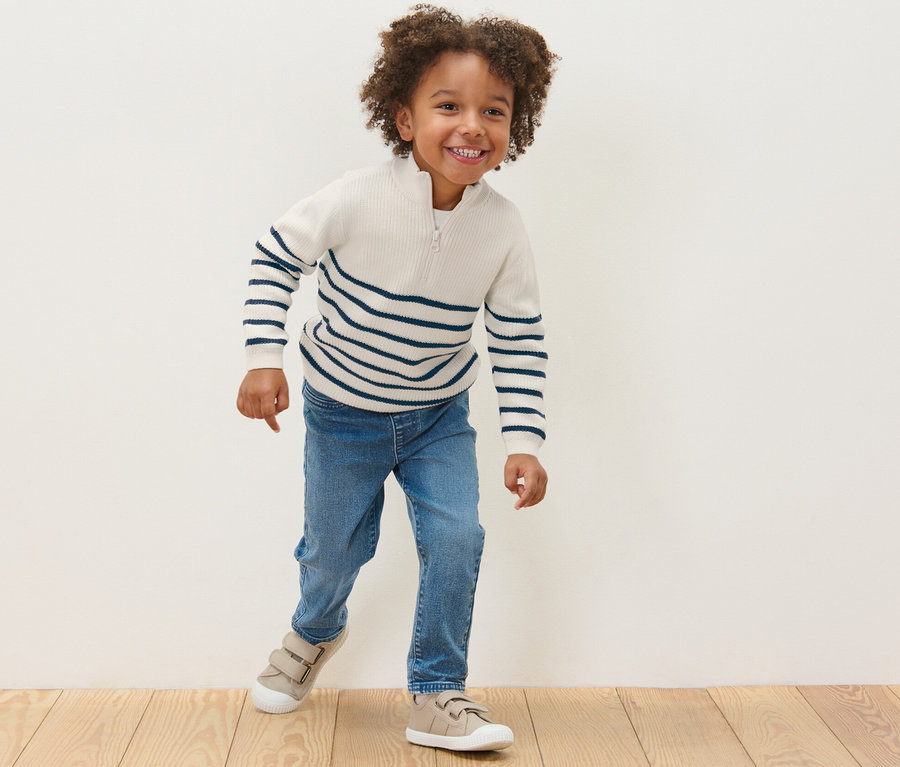 Lächelnder Junge trägt einen Kinder-Troyer mit blauen Streifen, Jeans und Turnschuhe.