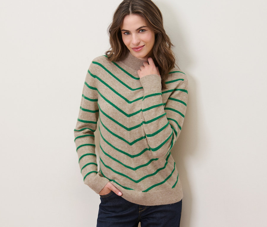 Frau posiert in einem creme-farbenen, gestreiften Strickpullover mit Stehkragen.