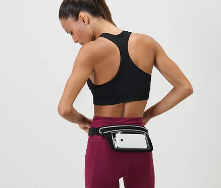 Frau justiert Laufgürtel für Smartphones um ihre Taille. Sie trägt einen Sport-BH und Leggings.