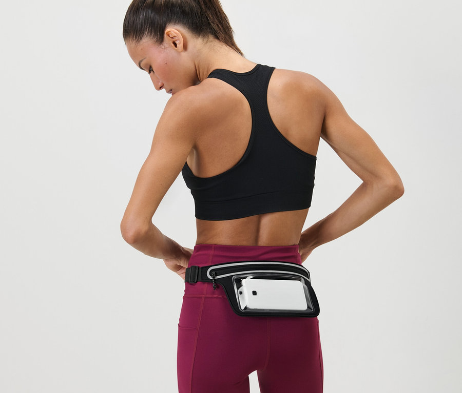 Frau justiert Laufgürtel für Smartphones um ihre Taille. Sie trägt einen Sport-BH und Leggings.