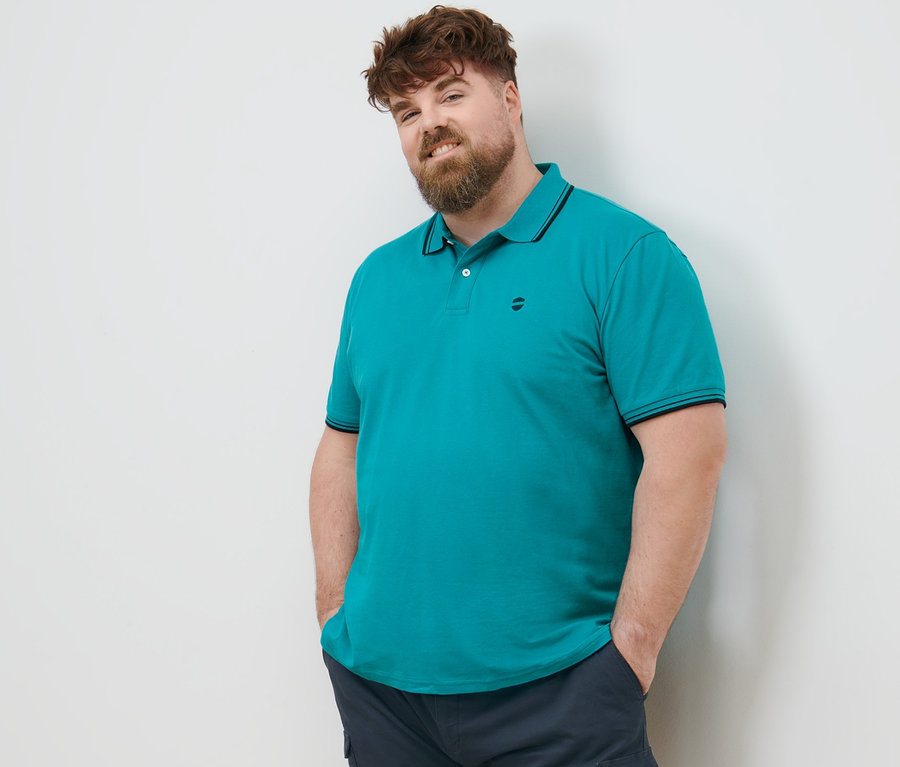 Ein Mann mit braunen Haaren steht mit den Händen in den Taschen seiner marineblauen Cargo-Shorts. Er trägt ein aqua Piqué-Poloshirt.