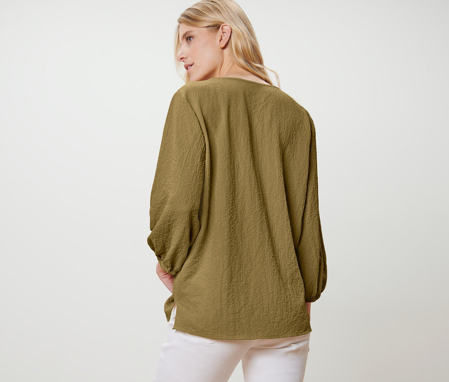 Eine Frau mit Tunika-Bluse steht mit dem Rücken zur Kamera.