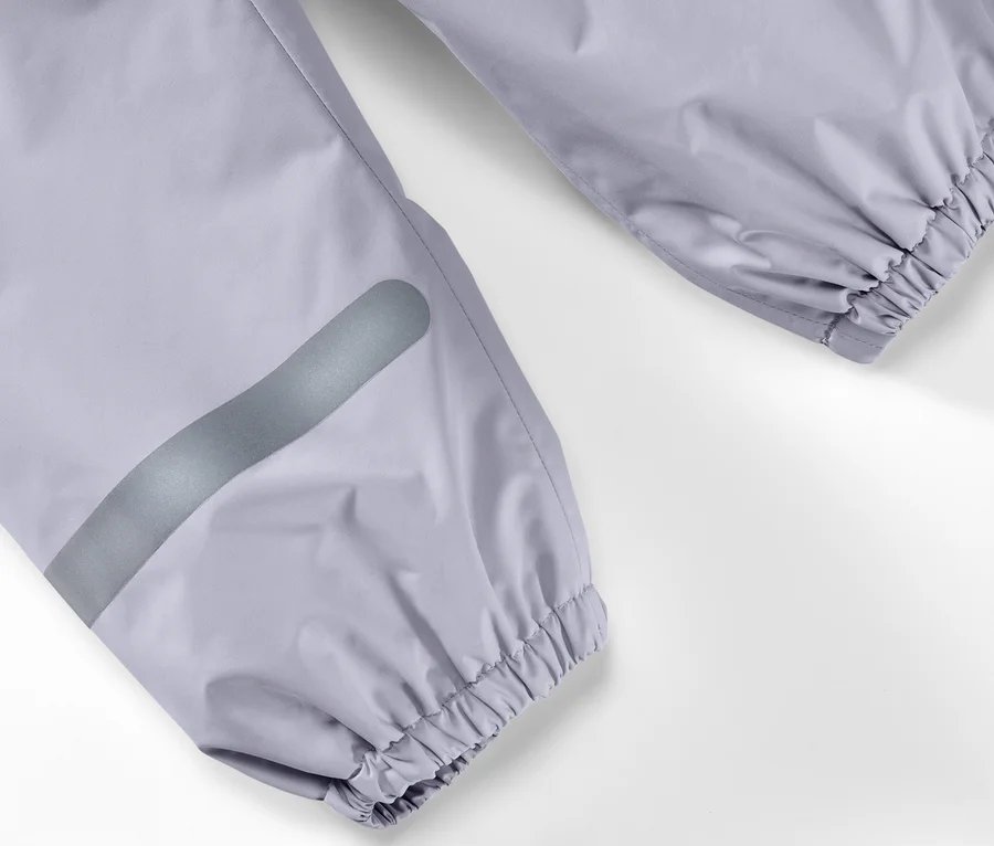 Detail einer Kinder-Regenhose mit silbernem Reflexstreifen am Bein und elastischem Saum am Knöchel.