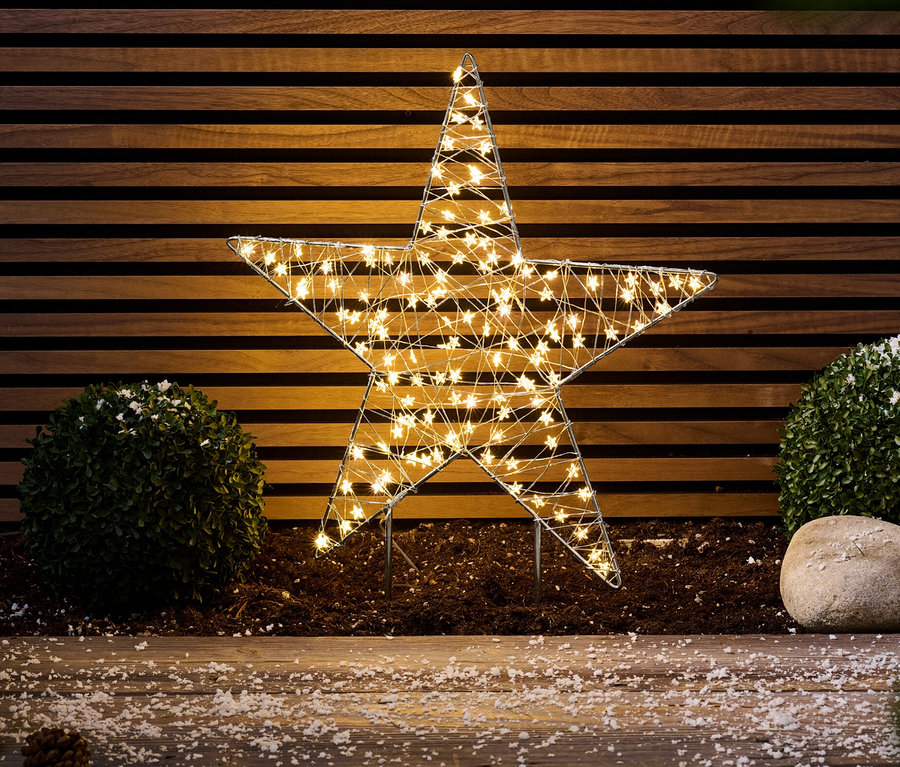 Ein Outdoor-LED-Stern steht vor einer Holzwand.