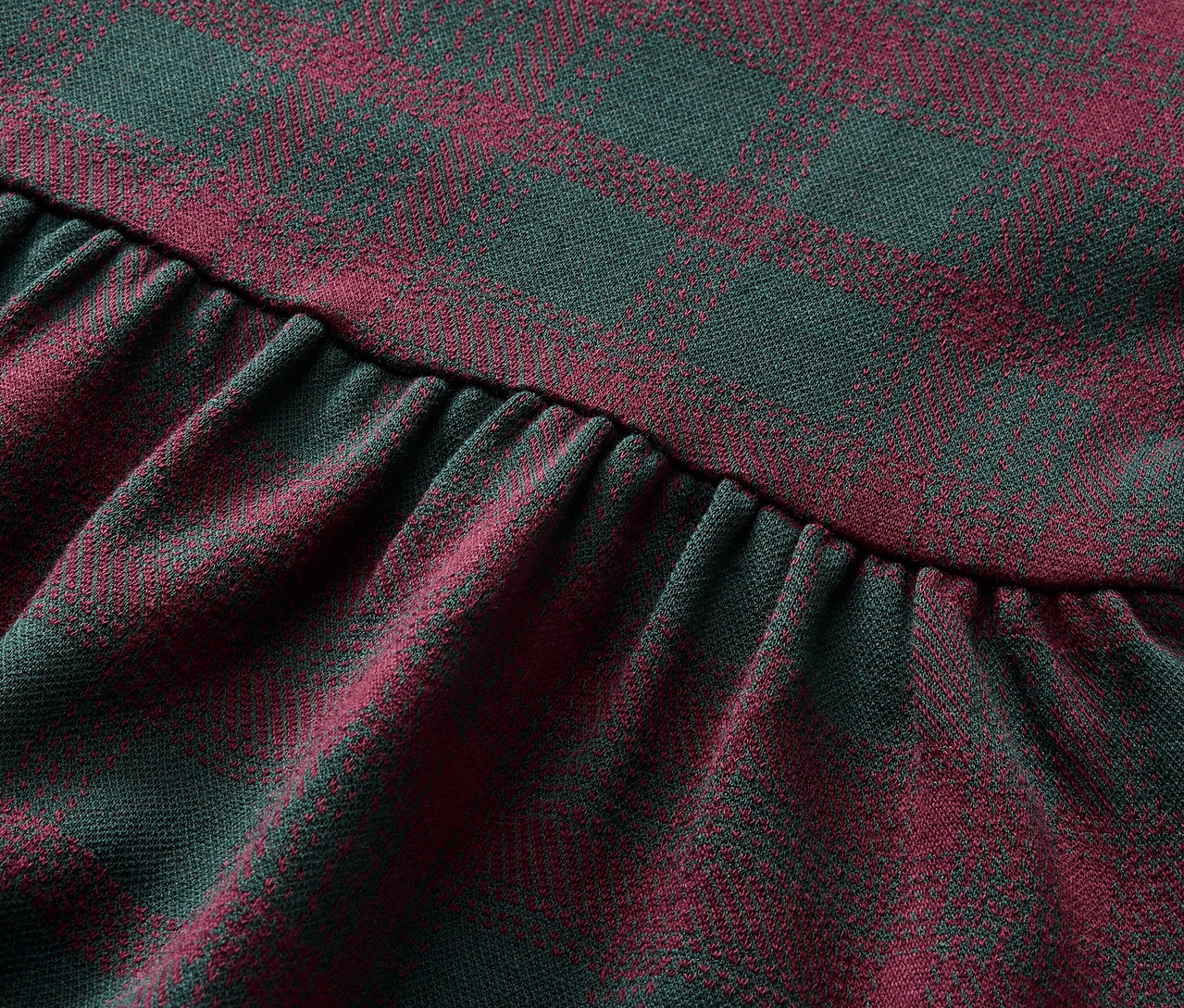 Detailaufnahme eines Stoffes mit rot-grünem Karomuster und Rüschen.