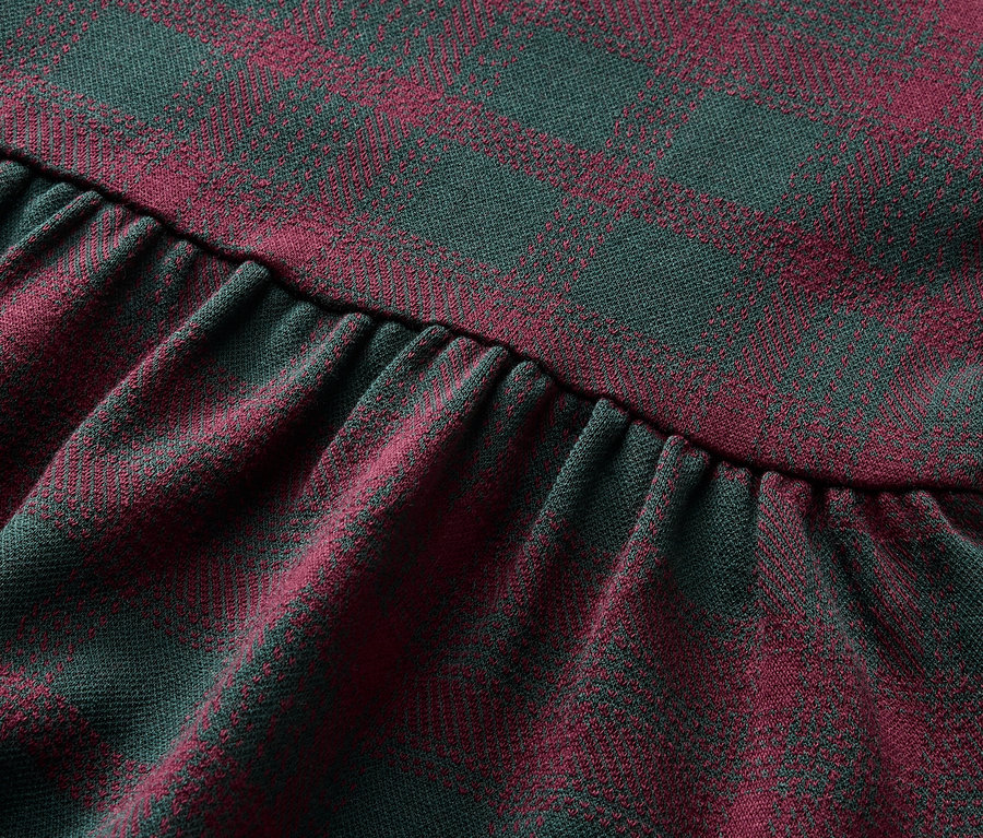 Detailaufnahme eines Stoffes mit rot-grünem Karomuster und Rüschen.