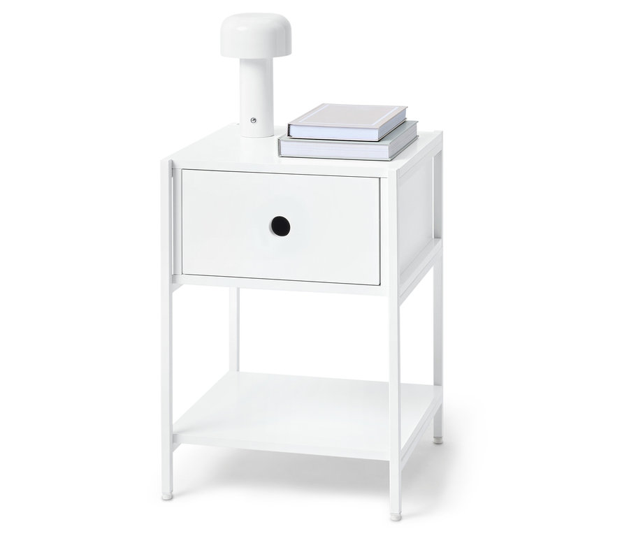 Weißer Nachttisch mit einer Schublade, einer Lampe und zwei Büchern oben drauf.