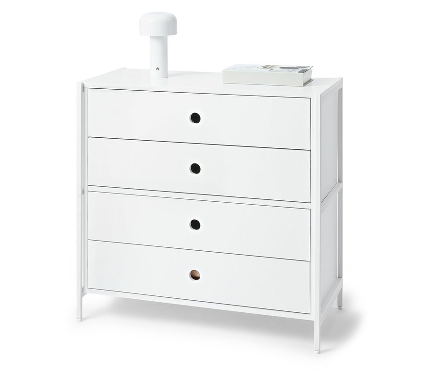 Weiße Kommode mit vier Schubladen, darauf eine Lampe und ein Buch.