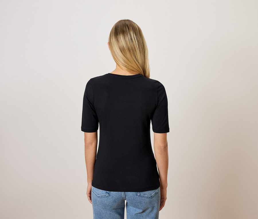Rückansicht einer blonden Frau in einem schwarzen T-Shirt und blauen Jeans.