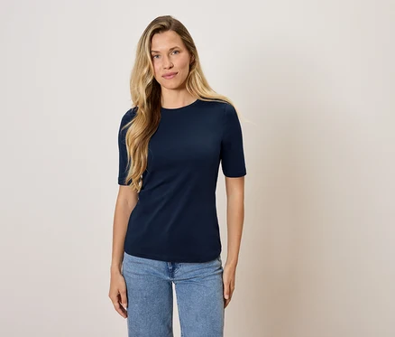 Eine Frau steht und trägt ein marineblaues T-Shirt und Jeans.