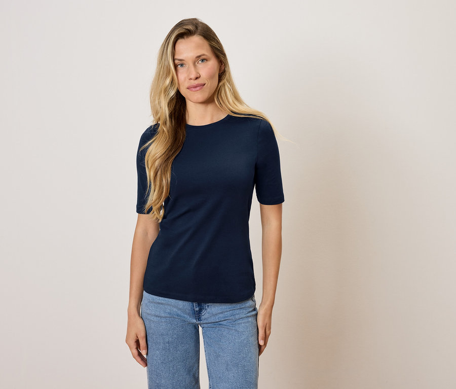 Eine Frau steht und trägt ein marineblaues T-Shirt und Jeans.