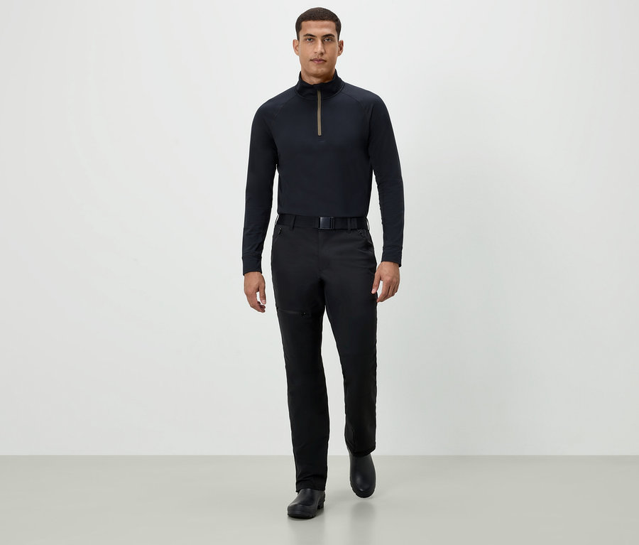 Ein Mann geht in einem schwarzen Langarmshirt, schwarzen Hosen und schwarzen Schuhen vorwärts.