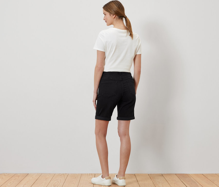 Frau von hinten mit Bermuda Jeans ‒ Fit »Lea«, black denim, weißem T-Shirt und Turnschuhen.