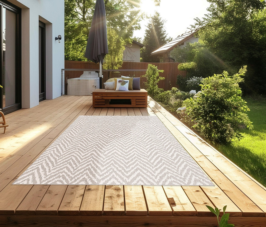 Outdoor-Teppich »Ecru Flow« mit Zickzackmuster auf Holzterrasse. Im Hintergrund Bank mit Kissen und Sonnenschirm.