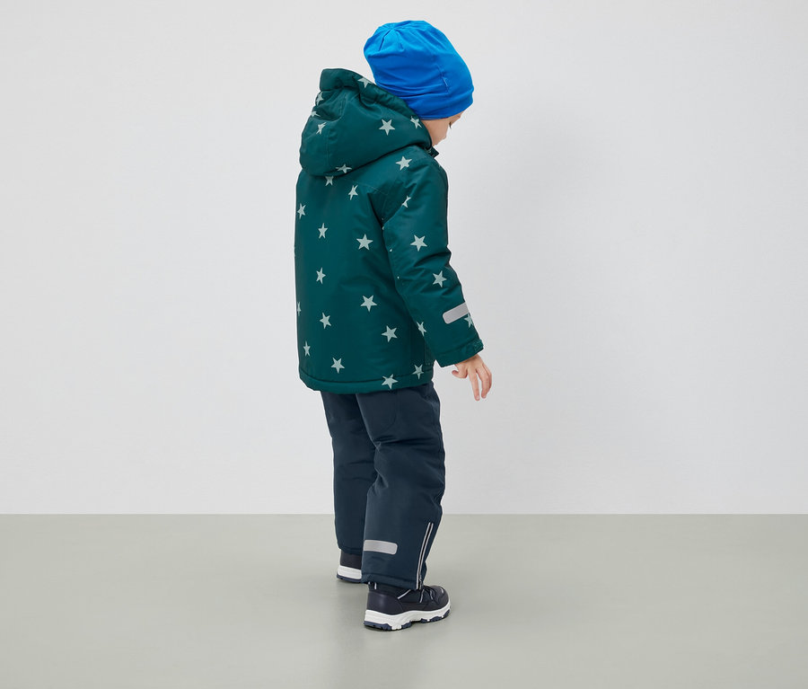 Junge mit dem Rücken zur Kamera trägt eine Winterjacke mit Sternmuster, eine blaue Mütze und dunkelblaue Hosen.