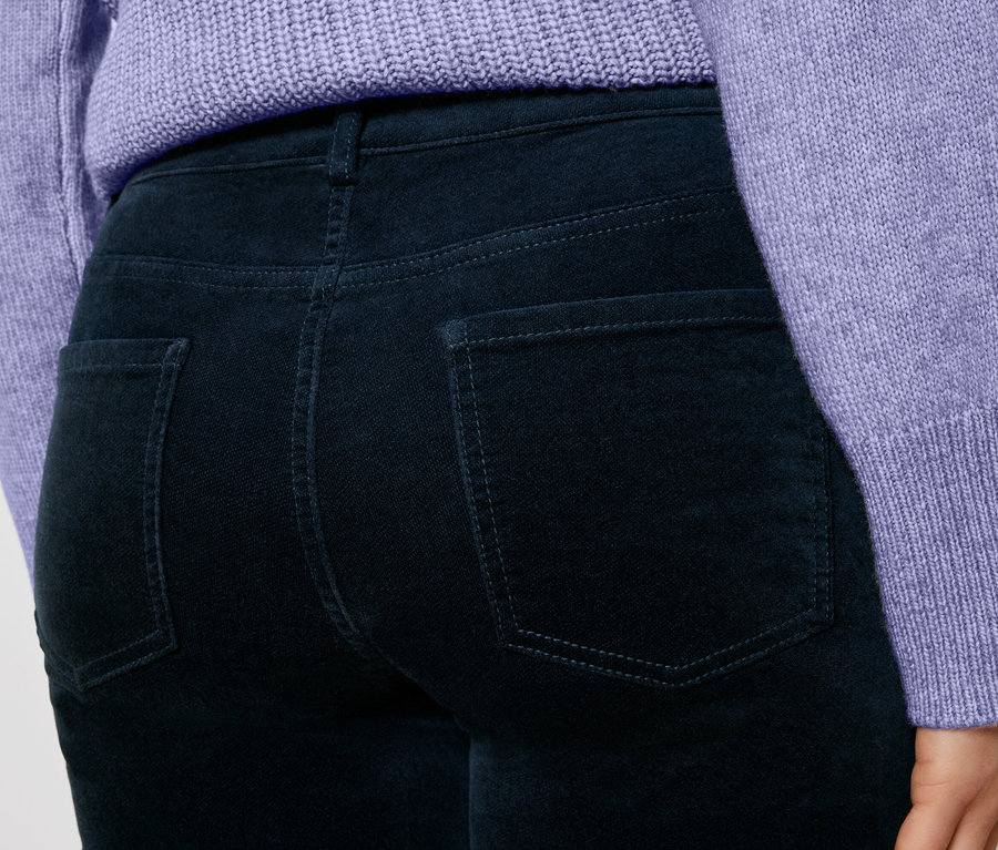 Detailaufnahme einer Frau, die dunkelblaue Cordhosen und einen lila Pullover trägt.