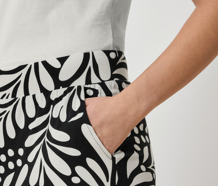 Nahaufnahme einer Person, die eine Hose mit einem schwarz-weißen Blattmuster und eine Hand in der Tasche trägt.