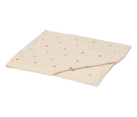 Eine cremefarbene Babydecke mit bunten Stickpunkten liegt gefaltet auf einer weißen Oberfläche.