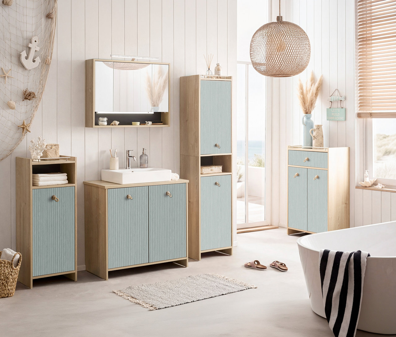 Badezimmer mit Waschtisch, Spiegelschrank, Hochschrank und Badewanne in Weiß und hellem Holz. Dekorationen im maritimen Stil.