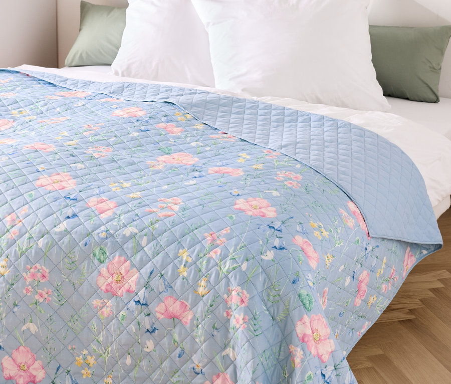 Blauer Überwurf mit Blumenmuster auf einem Bett mit weißen Kissen.