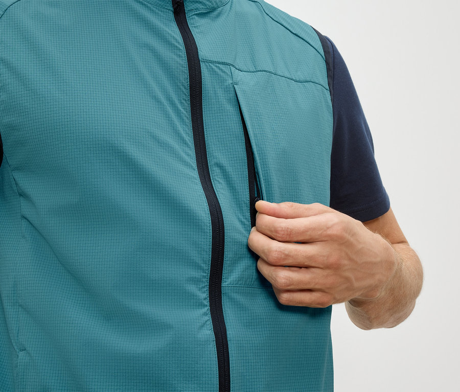 Mann öffnet die Reißverschlusstasche einer petrolfarbenen Weste.