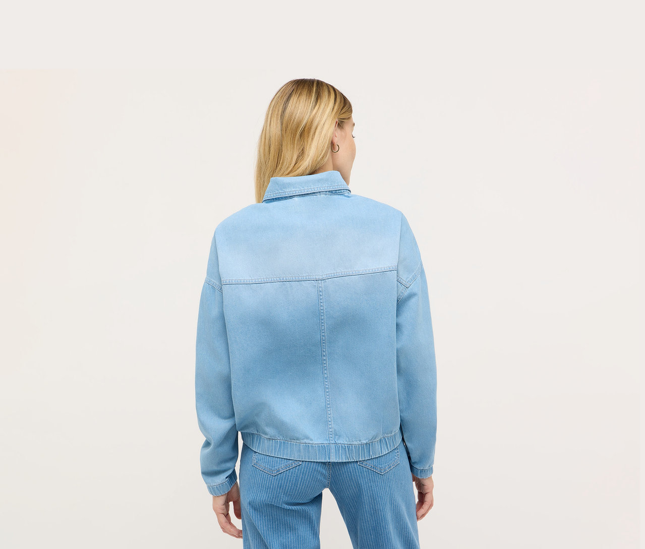 Rückansicht einer Frau mit blonden Haaren, die eine blaue Jeansjacke von Angels trägt.