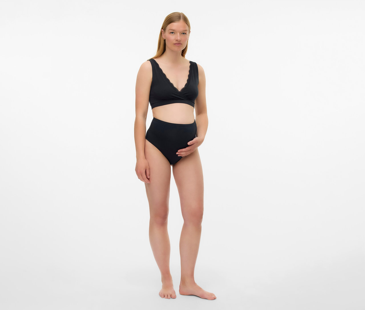 Schwangere Frau trägt schwarzen MAMALICIOUS 2er Pack Schwangerschafts-BH und hochgeschnittene Unterhose vor weißem Hintergrund.