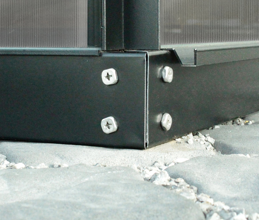 Nahaufnahme der Ecke des Vitavia Gewächshauses Orion ESG 3,8 m² inkl. Rahmenfundament, befestigt mit Schrauben auf Steinen.