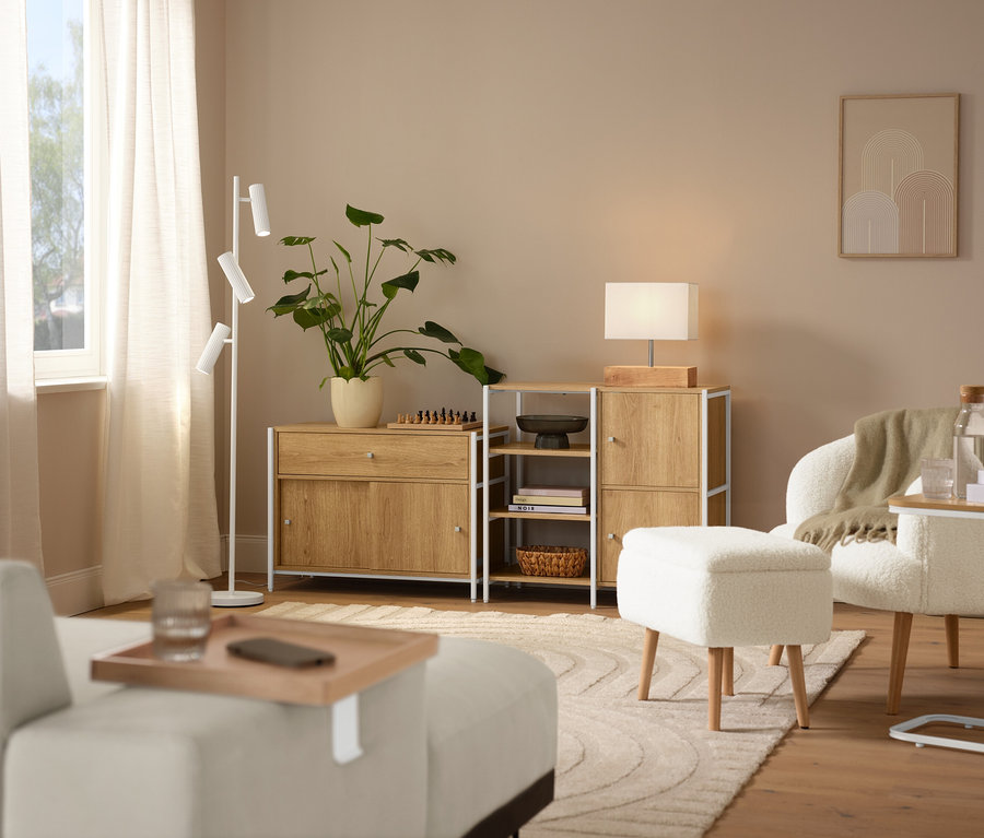 Einrichtungsszene mit einem beigen Teppich »Cosmo«, einem Bouclé-Sessel mit Holzbeinen, einem cremefarbenen DOMO Longchair, einer Trio Stehleuchte »Soka« und einer Tischleuchte mit Holzfuß.