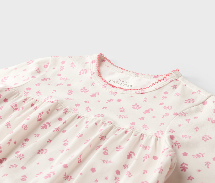 Nahaufnahme eines weißen Kinderkleides mit rosa Blumenmuster und rosa Saum am Halsausschnitt.