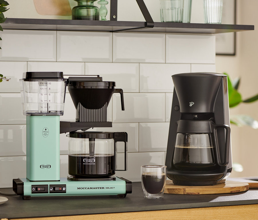 Zwei Kaffeemaschinen auf einer Küchentheke: eine pastellgrüne Moccamaster KBG Select Filterkaffeemaschine und eine schwarze.